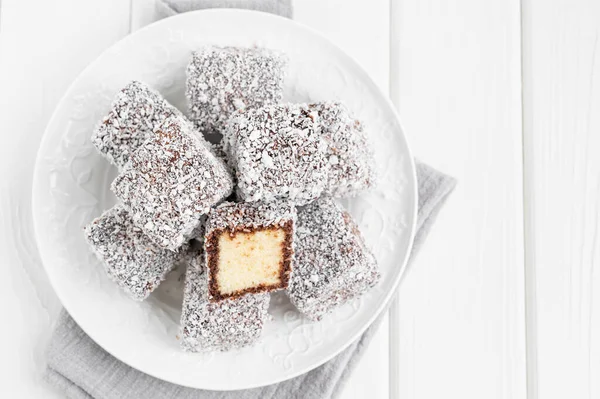 传统的澳大利亚拉明顿蛋糕 配上巧克力糖衣和椰子片 放在白色木制背景的白盘上 配上一杯茶 有选择的重点 — 图库照片