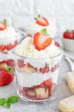 Çilekli tiramisu ya da ıvır zıvır, cam kavanozda tatlı, gri arka planda taze çilek ve nane yaprakları..