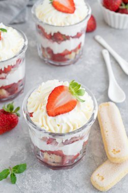 Çilekli tiramisu ya da ıvır zıvır, cam kavanozda tatlı, gri arka planda taze çilek ve nane yaprakları..