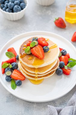 Beyaz bir tabakta gri beton bir zemin üzerinde böğürtlen ve bal bulunan bir yığın lezzetli pofuduk krep. Boşluğu kopyala