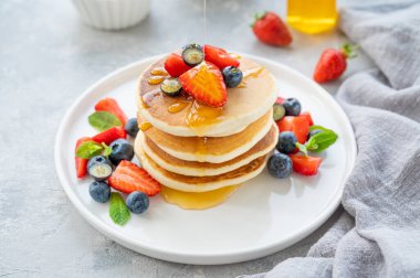 Beyaz bir tabakta gri beton bir zemin üzerinde böğürtlen ve bal bulunan bir yığın lezzetli pofuduk krep. Boşluğu kopyala