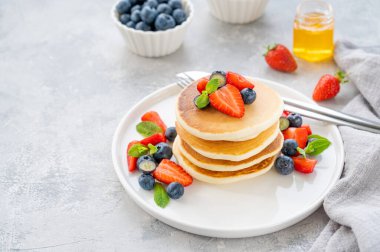 Beyaz bir tabakta gri beton bir zemin üzerinde böğürtlen ve bal bulunan bir yığın lezzetli pofuduk krep. Boşluğu kopyala