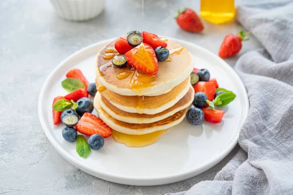 Beyaz bir tabakta gri beton bir zemin üzerinde böğürtlen ve bal bulunan bir yığın lezzetli pofuduk krep. Boşluğu kopyala
