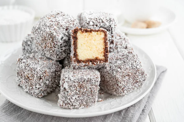 Geleneksel Avustralya Lamington pastası çikolatalı krema ve beyaz bir tabakta hindistan cevizi cipsi ve bir fincan çay. Seçici odak