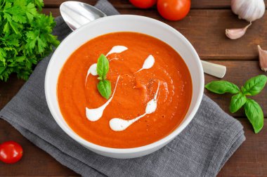 Koyu ahşap arka planda kremalı ve taze fesleğen yapraklı bir kasede domates çorbası püresi. Uzayı kopyala Üst görünüm