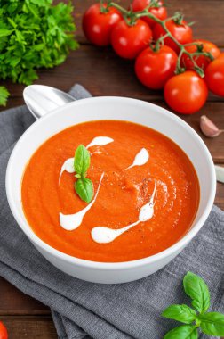 Koyu ahşap arka planda kremalı ve taze fesleğen yapraklı bir kasede domates çorbası püresi. Uzayı kopyala Üst görünüm