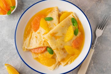 Turuncu şuruplu leziz krep Suzette ve gri beton arka planda meyveleri dilimliyor..