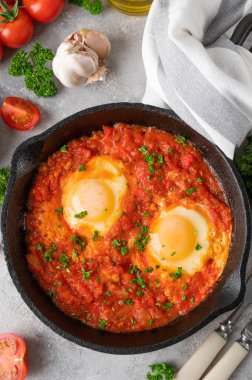 Shakshuka kızartma tavasında gri beton arka planda malzemelerle birlikte. Baharatlı ve taze maydanozlu domates soslu yumurta. Boşluğu kopyala