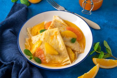 Portakal şurubuyla nefis krep Suzette ve mavi beton arka planda bir tabakta meyveleri dilimler..