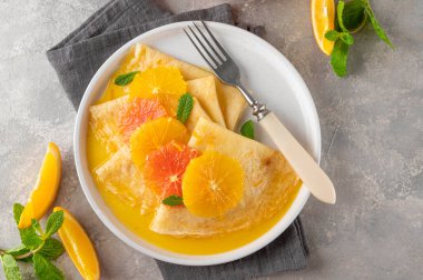 Turuncu şuruplu leziz krep Suzette ve gri beton arka planda meyveleri dilimliyor..