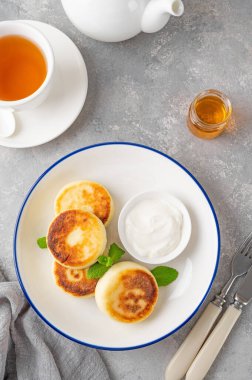 Süzme peynirli krep, şurup, ballı ricotta böreği ve gri beton arka planda ekşi krema. Sağlıklı ve lezzetli bir kahvaltı. Üst görünüm, alanı kopyala