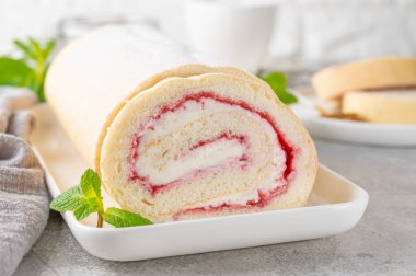 Gri arka planda beyaz bir tabakta çilek reçeli ve kremalı kek rulosu. Boşluğu kopyala
