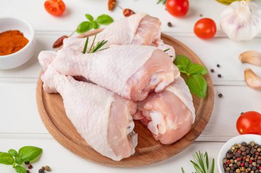 Çiğ tavuk budu beyaz ahşap bir arka planda kesim tahtasının üzerinde. Yemek yapmak için malzemeli et..