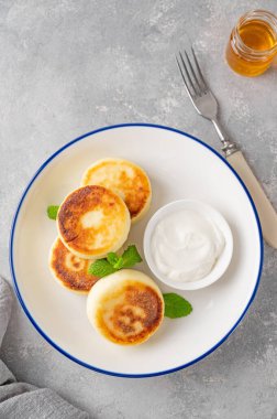 Süzme peynirli krep, şurup, ballı ricotta böreği ve gri beton arka planda ekşi krema. Sağlıklı ve lezzetli bir kahvaltı. Üst görünüm, alanı kopyala