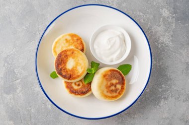 Cottage cheese pancakes, syrniki, ricotta fritters with honey and sour cream on a gray concrete background. Healthy and delicious breakfast. Top view, copy space
