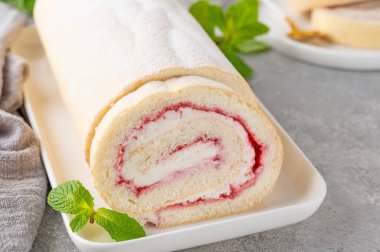 Gri arka planda beyaz bir tabakta çilek reçeli ve kremalı kek rulosu. Boşluğu kopyala