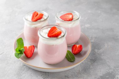 Strawberry mousse in a glass jar on a gray concrete background with whipped cream, fresh berries and mint leaves. Delicious summer dessert