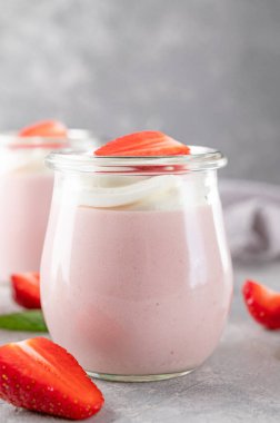 Strawberry mousse in a glass jar on a gray concrete background with whipped cream, fresh berries and mint leaves. Delicious summer dessert
