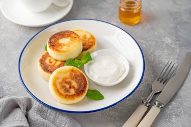 Cottage cheese pancakes, syrniki, ricotta fritters with honey and sour cream on a gray concrete background. Healthy and delicious breakfast. Top view, copy space