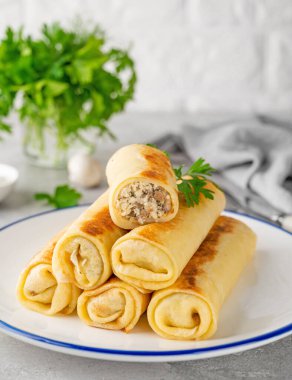 Pancakes or thin crepes stuffed with chicken and mushrooms on a plate on a gray concrete background. Selective focus, copy space