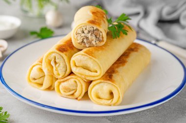 Pancakes or thin crepes stuffed with chicken and mushrooms on a plate on a gray concrete background. Selective focus, copy space