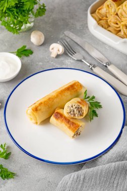 Pancakes or thin crepes stuffed with chicken and mushrooms on a plate on a gray concrete background. Selective focus, copy space