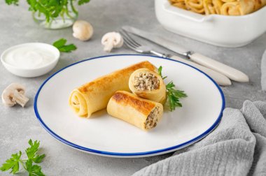 Pancakes or thin crepes stuffed with chicken and mushrooms on a plate on a gray concrete background. Selective focus, copy space