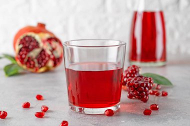 A glass of pomegranate juice with fresh pomegranate fruits on a gray concrete background. Vitamins and minerals. Healthy drink concept. Copy space