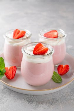 Strawberry mousse in a glass jar on a gray concrete background with whipped cream, fresh berries and mint leaves. Delicious summer dessert