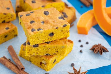 Pumpkin blondie or cake with chocolate drops, walnuts, cinnamon and anise on baking paper on a blue concrete background. Dessert for Thanksgiving or Halloween