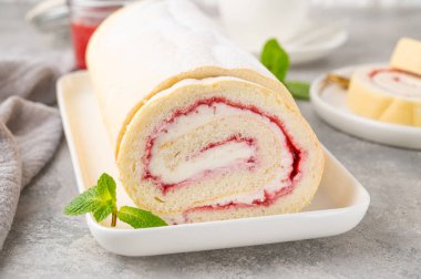 Gri arka planda beyaz bir tabakta çilek reçeli ve kremalı kek rulosu. Boşluğu kopyala