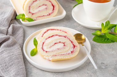 Gri arka planda beyaz bir tabakta çilek reçeli ve kremalı kek rulosu. Boşluğu kopyala