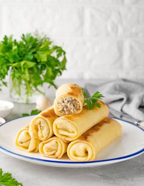 Pancakes or thin crepes stuffed with chicken and mushrooms on a plate on a gray concrete background. Selective focus, copy space