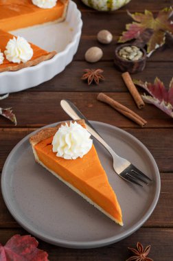 Traditional pumpkin pie with whipped cream and cinnamon on dark wooden background. Homemade pastry for Thanksgiving or Halloween. Copy space