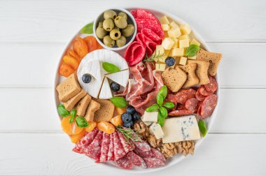 Çeşitli peynirli Charcuterie tahtası, salam, korizzo, prosciutto, bal, üzüm, fındık, zeytin, ekmek, yabanmersini ve beyaz ahşap arka planda taze otlar. Şenlikli bir atıştırmalık