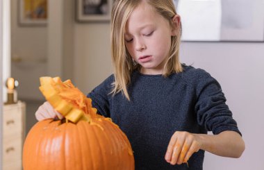 Balkabağı oyan ve ellerini kirleten mutlu sarışın çocuk. Kirli ellere odaklan. Cadılar Bayramı konsepti