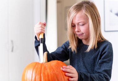 Balkabağı oyan ve ellerini kirleten mutlu sarışın çocuk. Kirli ellere odaklan. Cadılar Bayramı konsepti