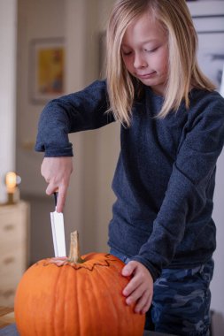 Balkabağı oyan ve ellerini kirleten mutlu sarışın çocuk. Kirli ellere odaklan. Cadılar Bayramı konsepti