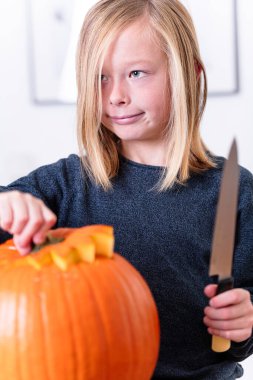 Balkabağı oyan ve ellerini kirleten mutlu sarışın çocuk. Kirli ellere odaklan. Cadılar Bayramı konsepti