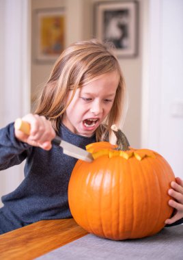 Balkabağı oyan ve ellerini kirleten mutlu sarışın çocuk. Kirli ellere odaklan. Cadılar Bayramı konsepti