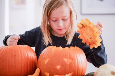 Balkabağı oyan ve ellerini kirleten mutlu sarışın çocuk. Kirli ellere odaklan. Cadılar Bayramı konsepti