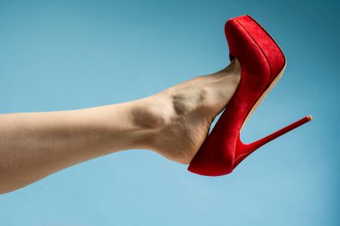 woman foot in stylish red High heels shoe against blue studio background 