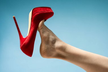 woman foot in stylish red High heels shoe against blue studio background 