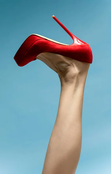 woman foot t in stylish red High heels shoe against blue studio background