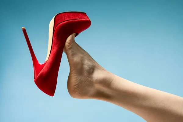 woman foot in stylish red High heels shoe against blue studio background