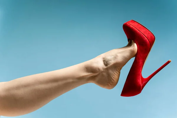 woman foot in stylish red High heels shoe against blue studio background