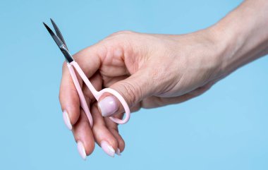 female hand holding manicure scissors against blue background 