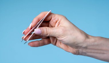 cropped image of female hand holding tweezers against blue background 