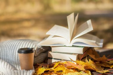 Sonbahar okuması, bir yığın kitap sarı yaprakların arkasında sıcak bir eşarp ve sıcak bir kahvenin yanında yatıyor.
