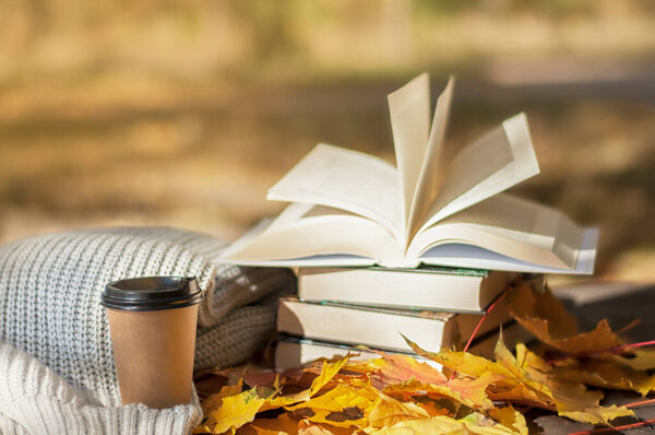 Осеннее чтение, стопка книг лежит рядом теплый шарф и горячий кофе на фоне желтых листьев